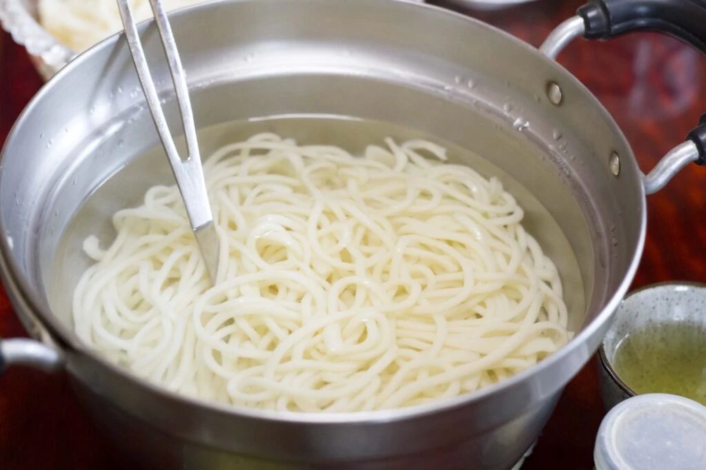鍋で茹で上げたそうめんをトングで持ち上げる様子