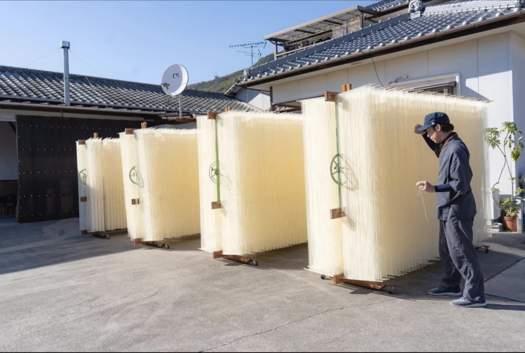 屋外に並ぶマルカツ製麺所の手延べそうめんの大型の干し簾と職人