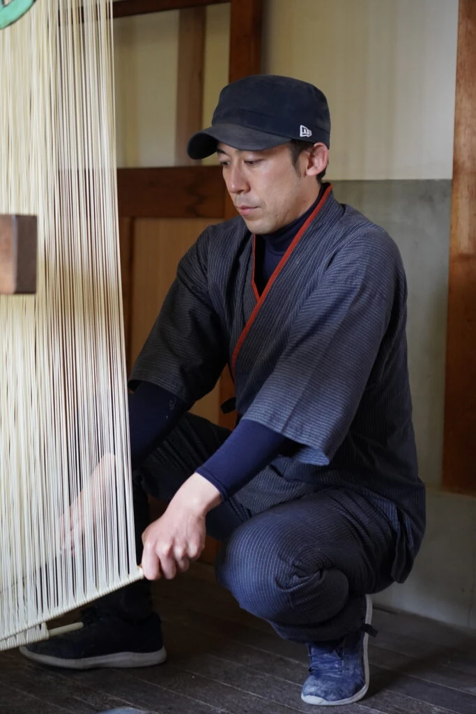 マルカツ製麺所で手延べそうめんの掛巻作業を行う作務衣姿の職人