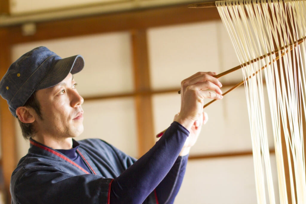 マルカツ製麺所で作務衣姿の職人が手延べそうめんを箸で分ける様子
