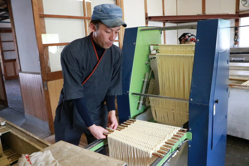 マルカツ製麺所で製麺機を使い手延べそうめんの掛巻作業をする職人